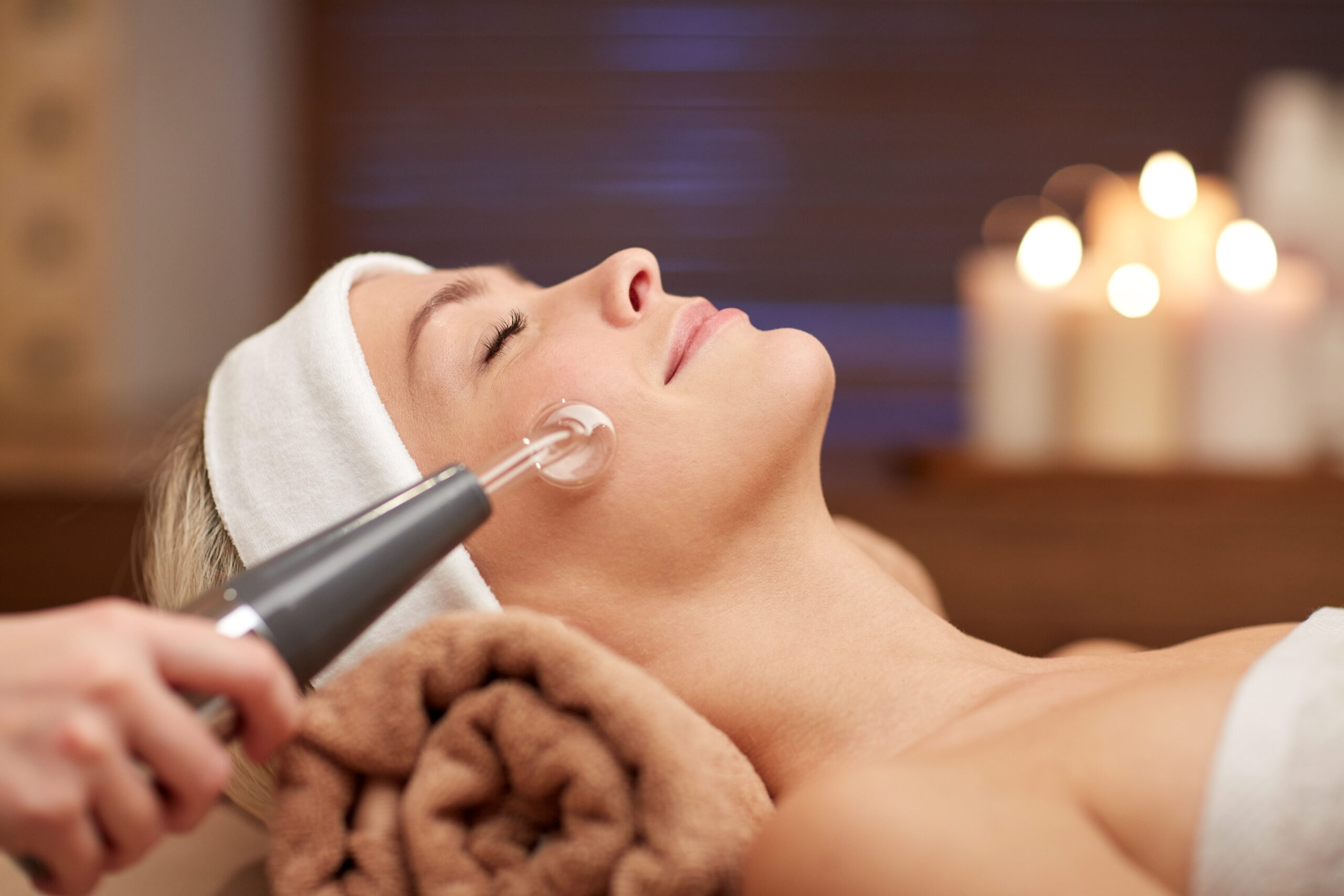 people, beauty, spa, cosmetology and technology concept - close up of beautiful young woman lying with closed eyes having face massage by massager in spa