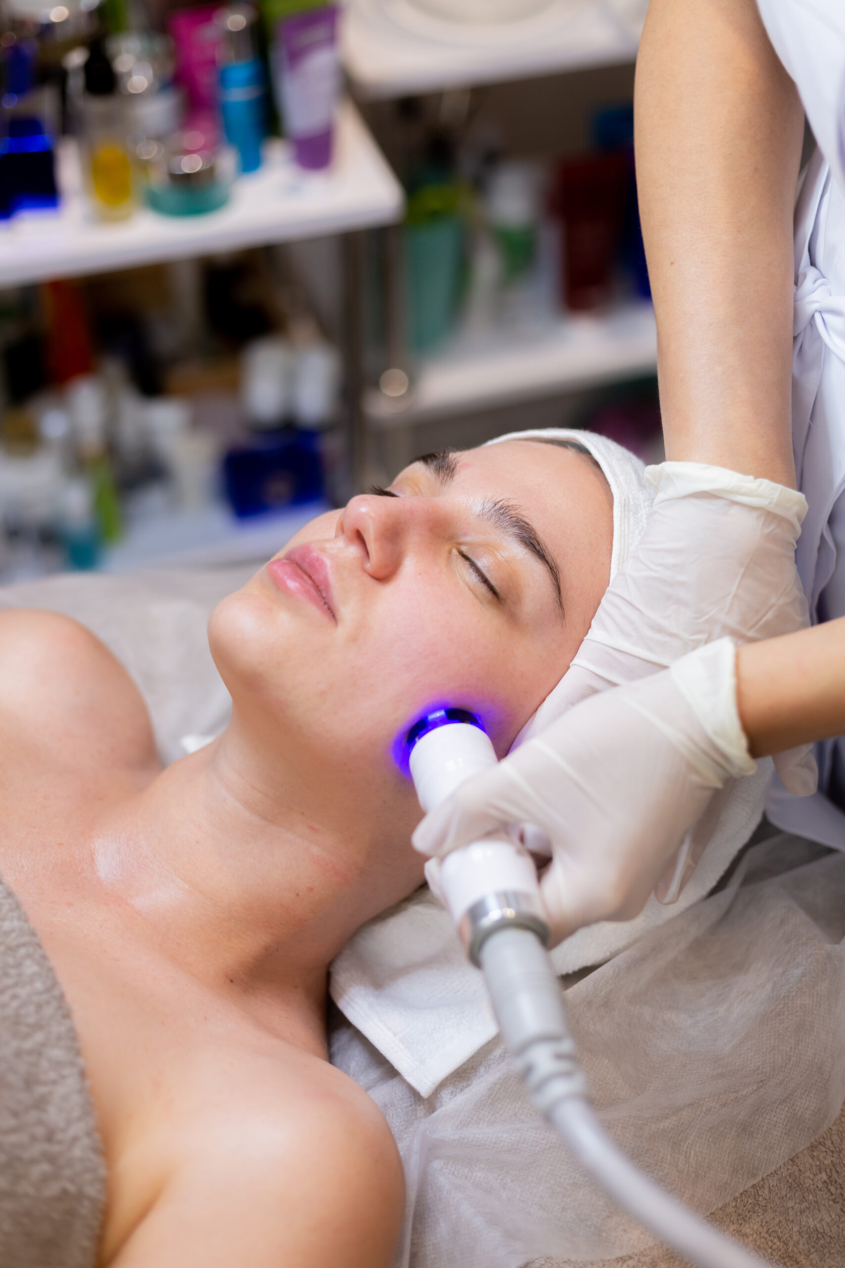 A young beautiful girl lies on the beautician's table and receives procedures with a professional apparatus for skin rejuvenation and moisturizing